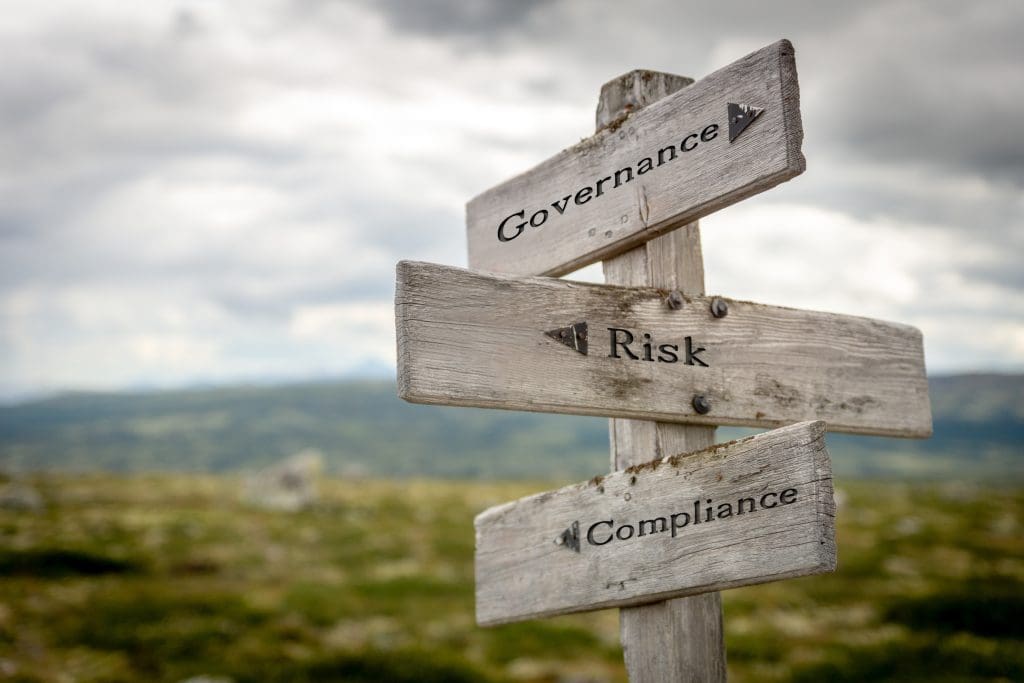 A wooden post sign with three boards that read Governance, Risk, Compliance.
