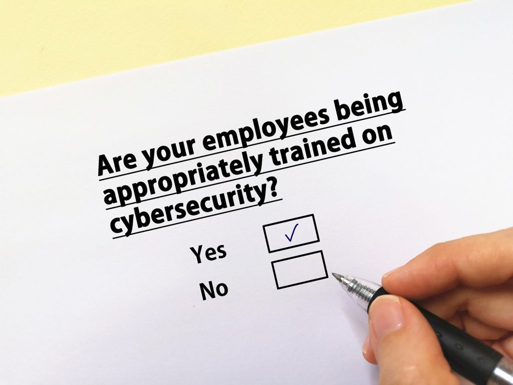 A piece of paper with a question about cybersecurity training and a person holding a pen checking yes.