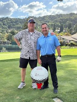 Two men standing behind a poster shaped like a golf ball that says "PC Professional"