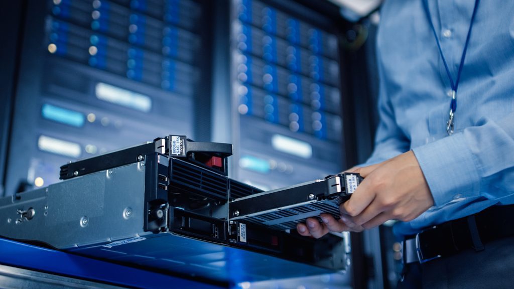 An IT professional in a server room placing a hard drive into a slot.