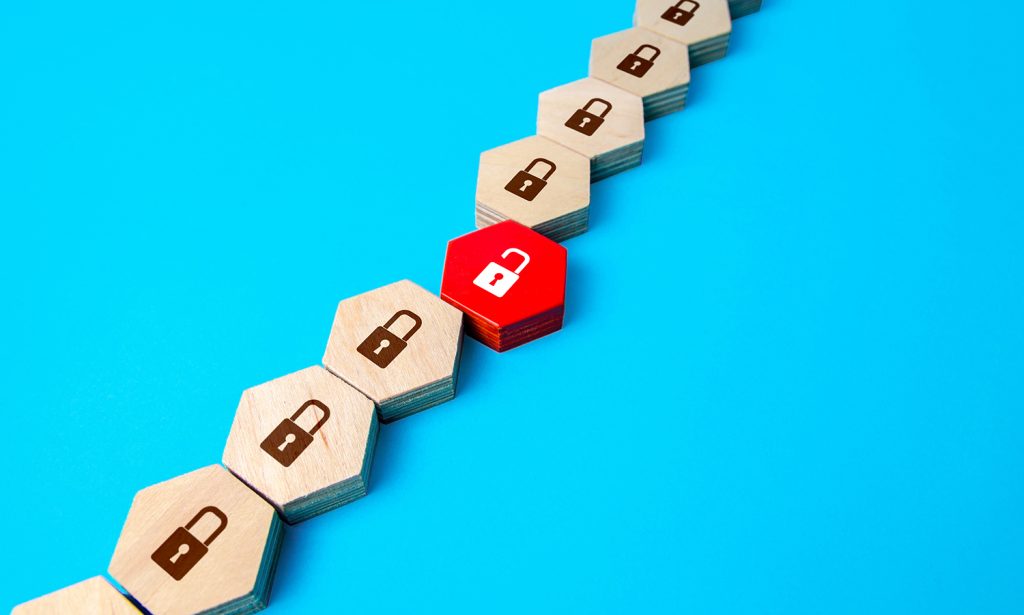 A row of wooden hexagon blocks with locks printed on top – one is painted red with a white unlocked padlock painted on top, and is out of sequence with the others.